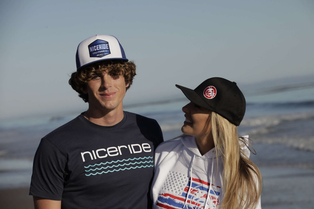 Young couple wearing stylish hats and casual beachwear, enjoying the fresh air by the ocean on a bright sunny day.