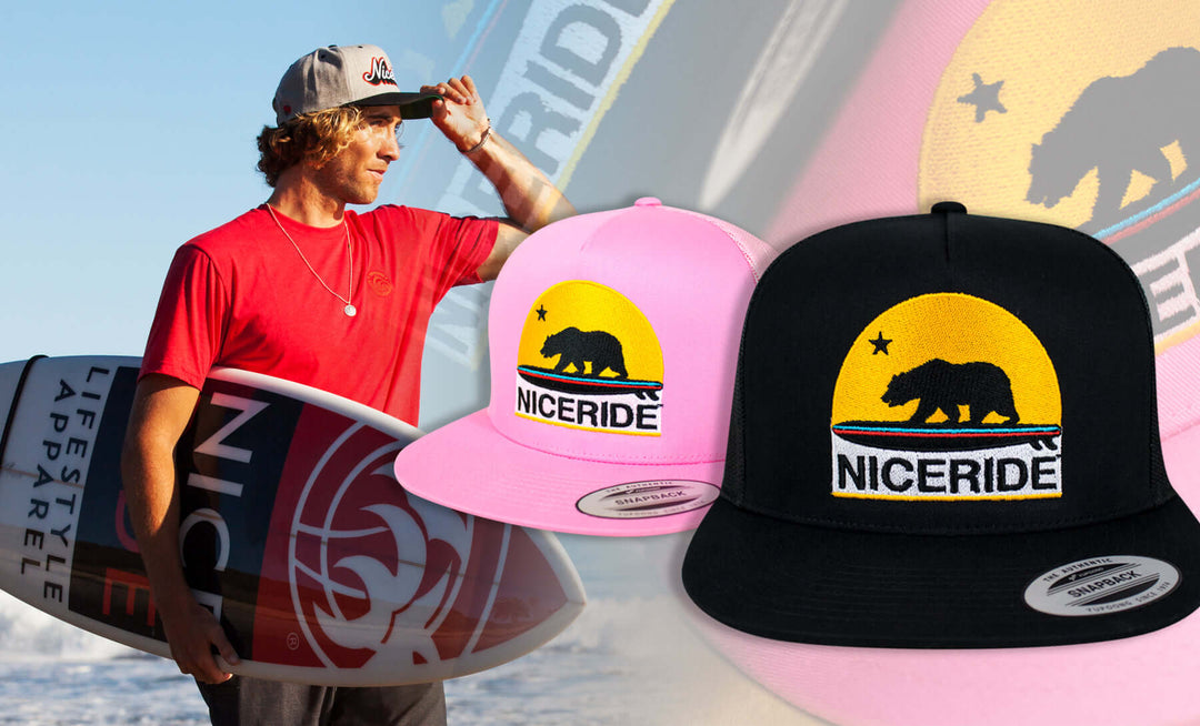 A surfer holding a surfboard next to Niceride branded hats in black and pink.