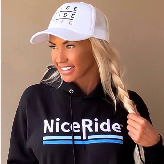 Woman wearing a hoodie with NiceRide logo and a white cap, embracing the cozy vibe of hoodie season.