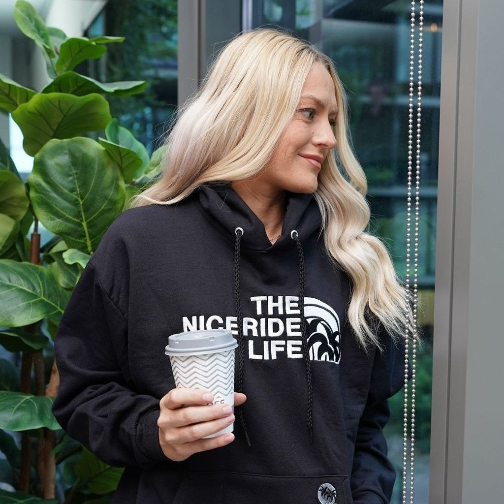 Woman in a black hoodie holding coffee cup, showcasing hoodies as stylish and comfortable wear year-round.