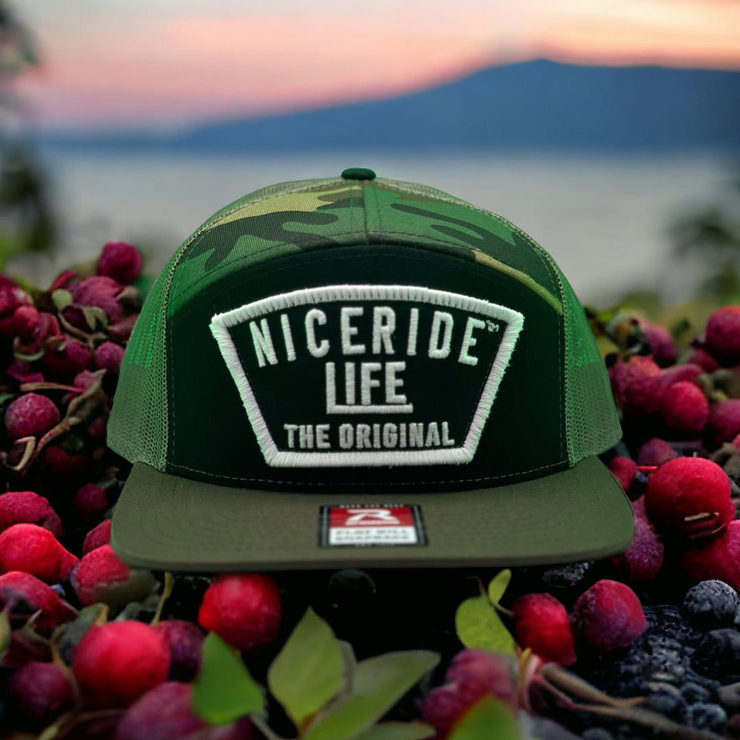 Green camo Niceride hat displayed on vibrant berries, showcasing outdoor style and brand identity.