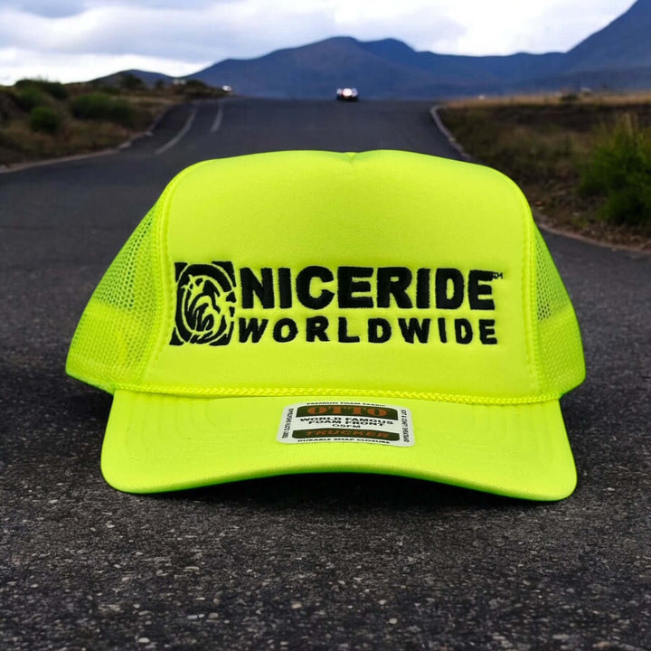NICERIDE Worldwide bright yellow foam trucker hat on a road with mountains in the background.