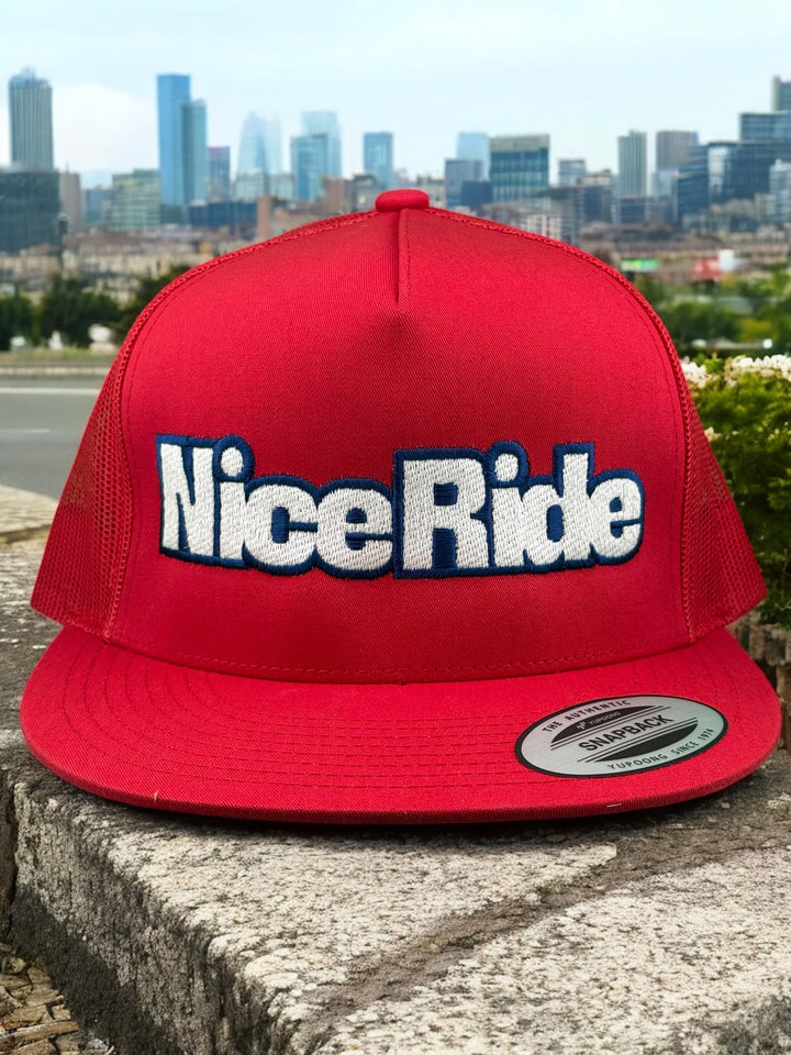 Red unisex adjustable trucker hat featuring the embroidered "Nice Ride" logo in bold, set against a city skyline backdrop.