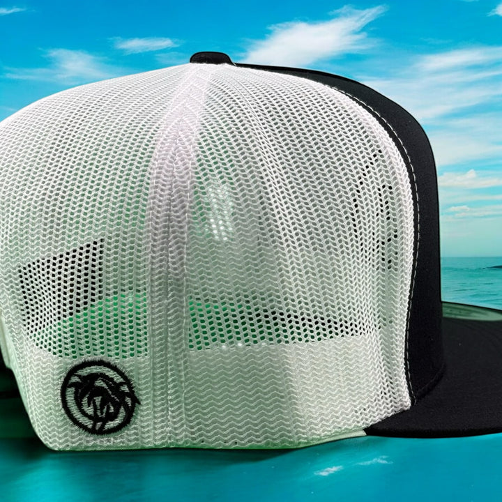 Back view of "Trading" 6006 unisex adjustable trucker hat with NICERIDE logo, in front of a scenic ocean background.
