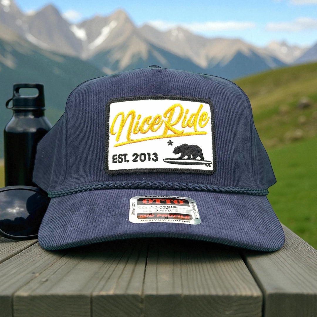 "Big Sky" corduroy snapback baseball cap with NiceRide logo against mountain backdrop.