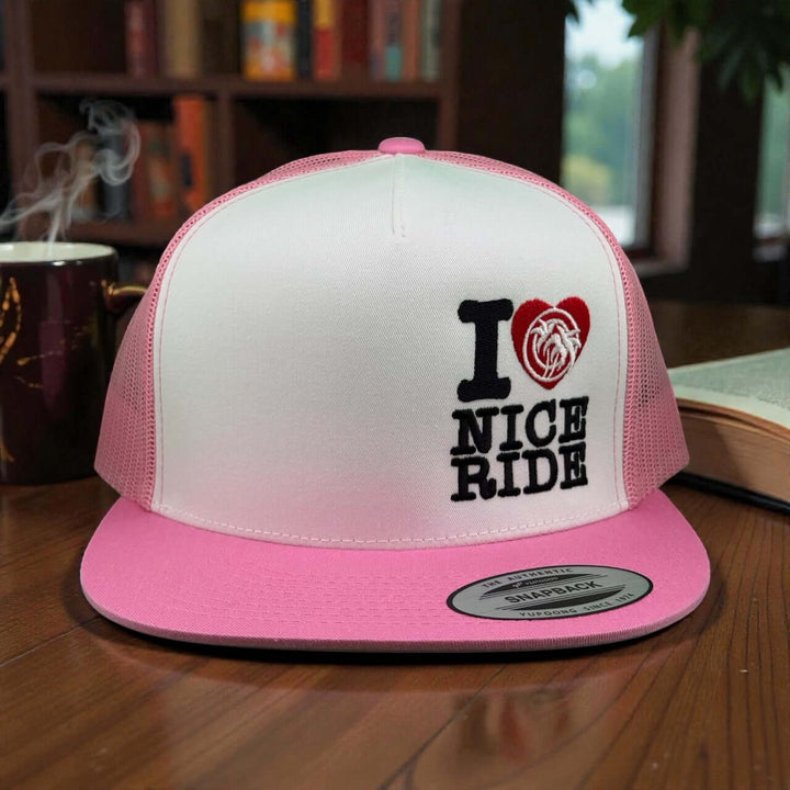 IHEART 6006 Unisex Trucker Hat in pink with embroidered I LOVE NICE RIDE design on a table.