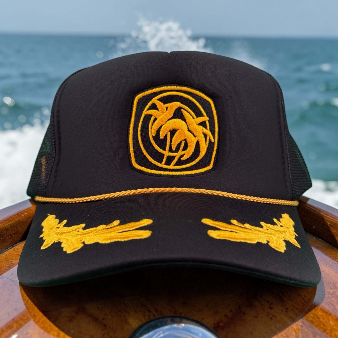 Below Deck Moe Doe hat on a boat with ocean in background, showcasing palm tree logo and vibrant colors.