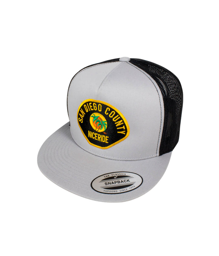 The Badge hat featuring San Diego County NICERIDE embroidered design on a gray snapback trucker cap.