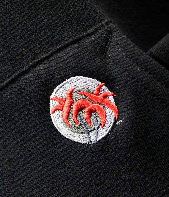 Close-up of the NICERIDE palm logo embroidered on the pocket of a black pullover hoodie.