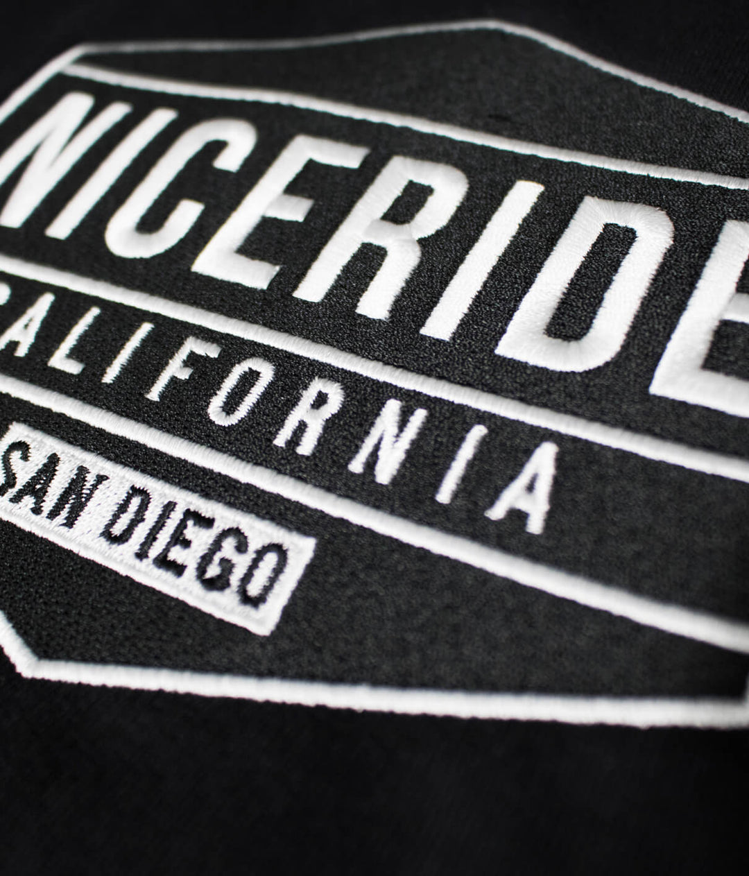 Close-up of NICERIDE California logo embroidered on black hoodie fabric.