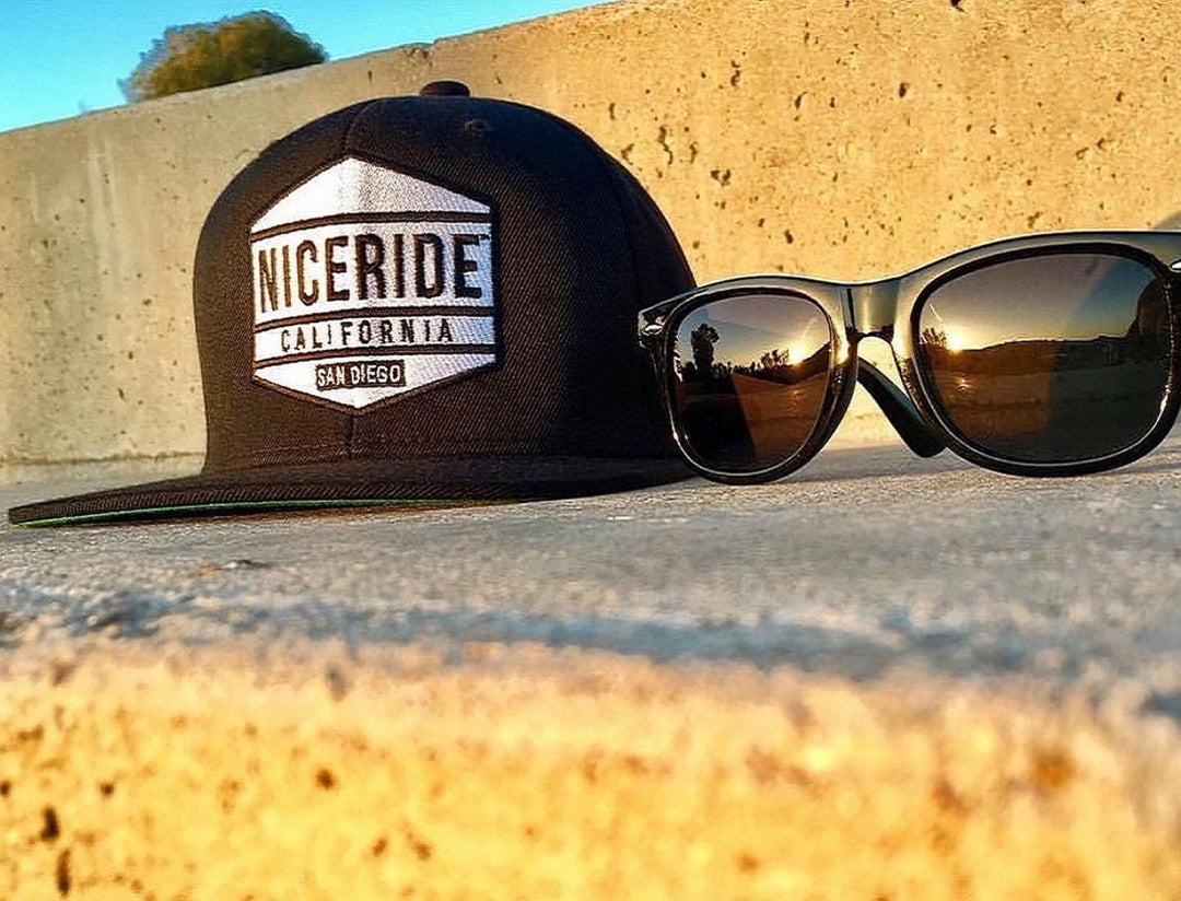 Good Times snapback hat resting next to sunglasses on a smooth surface, showcasing NICERIDE California design.