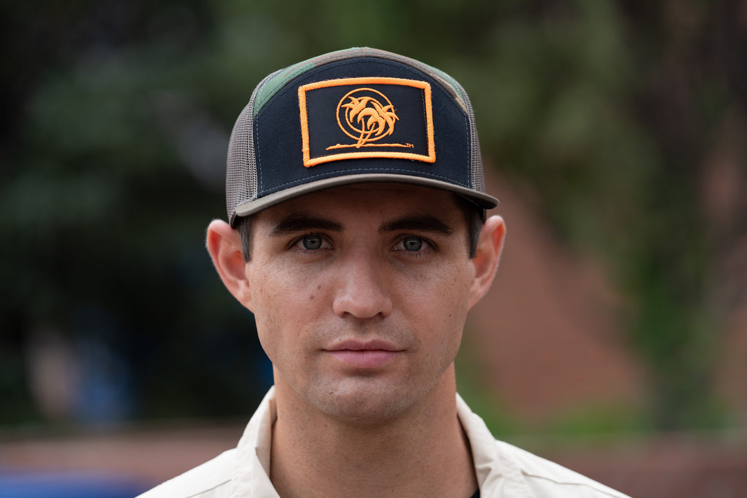 Man wearing a "Palm Patch" 7 Panel Trucker Snapback Cap, front view showcasing neon orange embroidery.