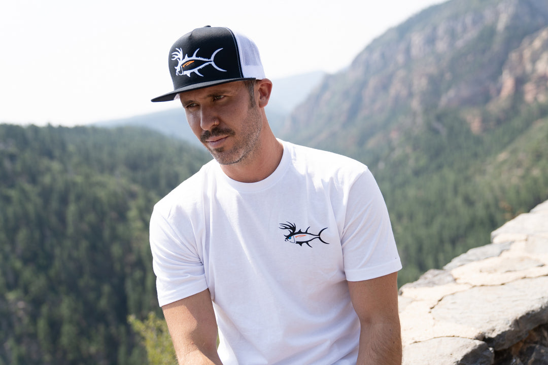 Man wearing a white shirt and black-and-white hat outdoors, showcasing outdoor style and lifestyle in nature.