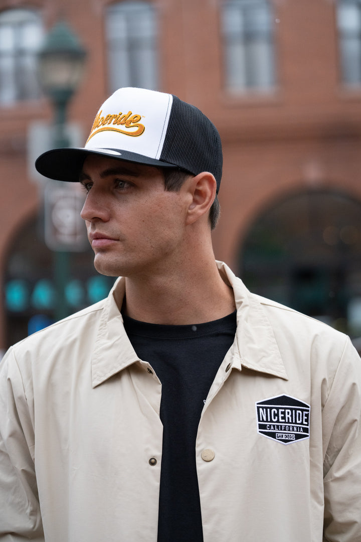 Model wearing a NICERIDE windbreaker jacket with logo and baseball cap in an urban setting.