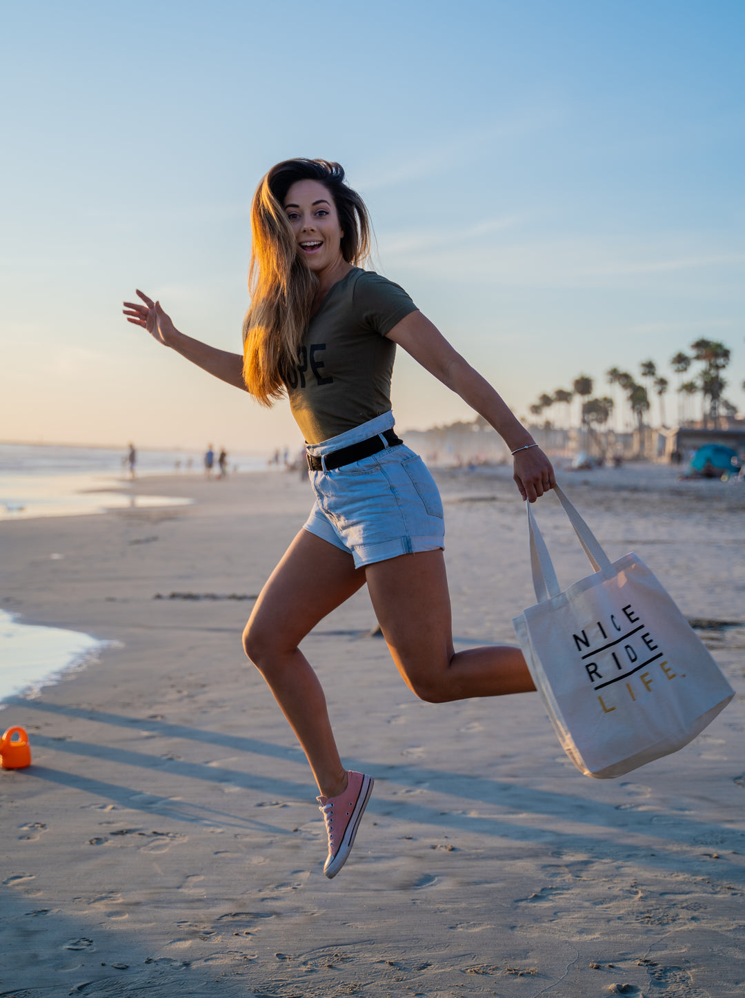 Woman running on the beach carrying a La Jolla tote bag, enjoying a sunny day by the water.