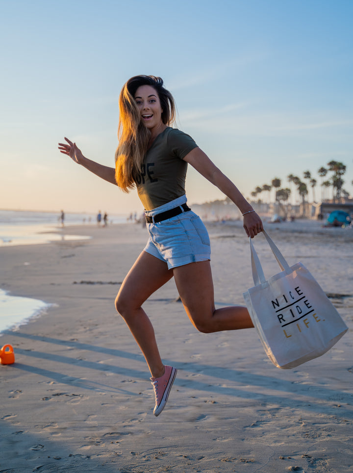 Woman running on the beach carrying a La Jolla tote bag, enjoying a sunny day by the water.
