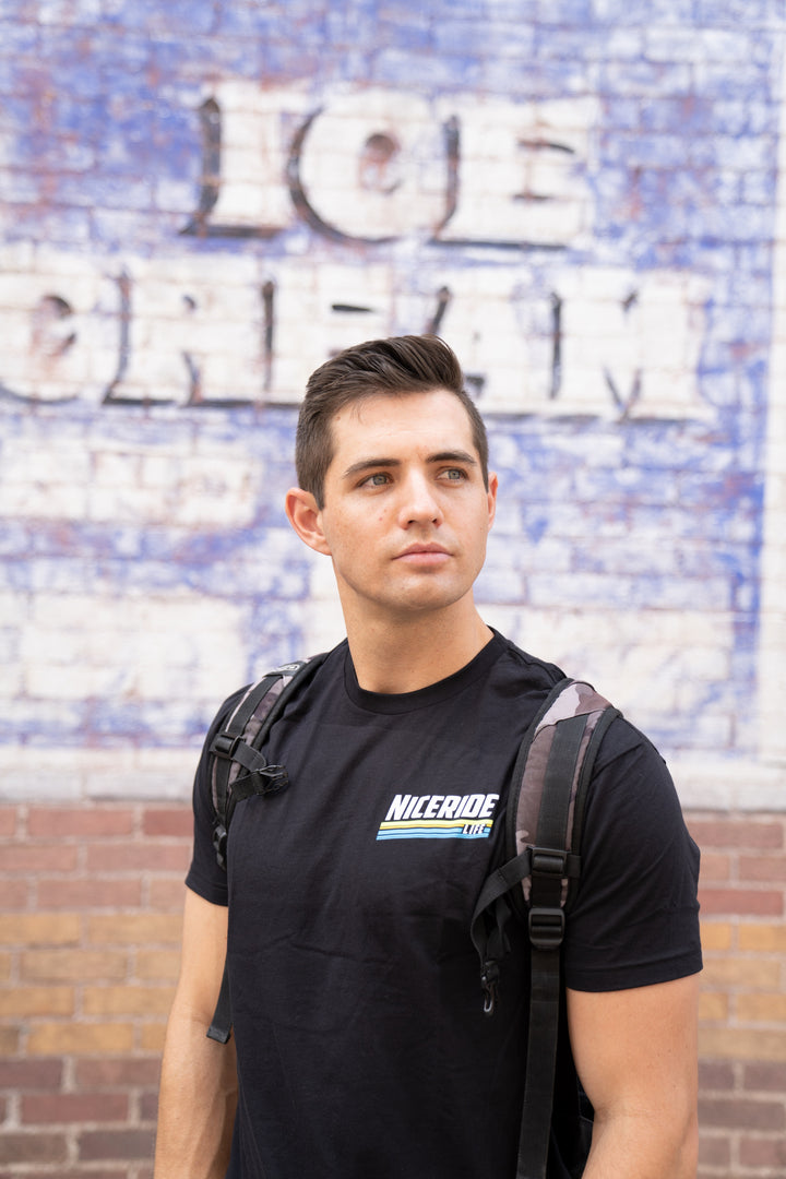 Man wearing a black shirt from NICERIDE standing against an ice cream shop wall.